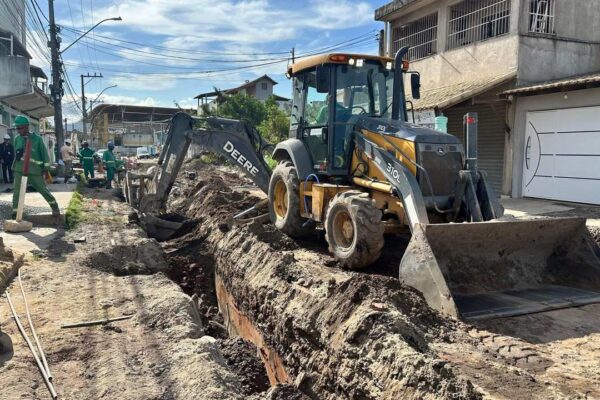 Retroescavadeira Deere 310L em obras de saneamento, com operários trabalhando em rua.