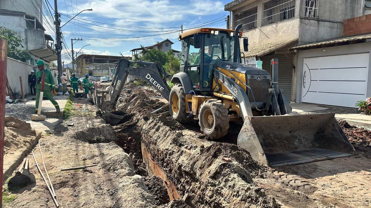 Retroescavadeira Deere 310L em obras de saneamento, com operários trabalhando em rua.
