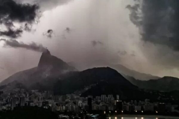 Rio de Janeiro sob tempestade, com o Cristo Redentor visível, céu nublado e chuva.
