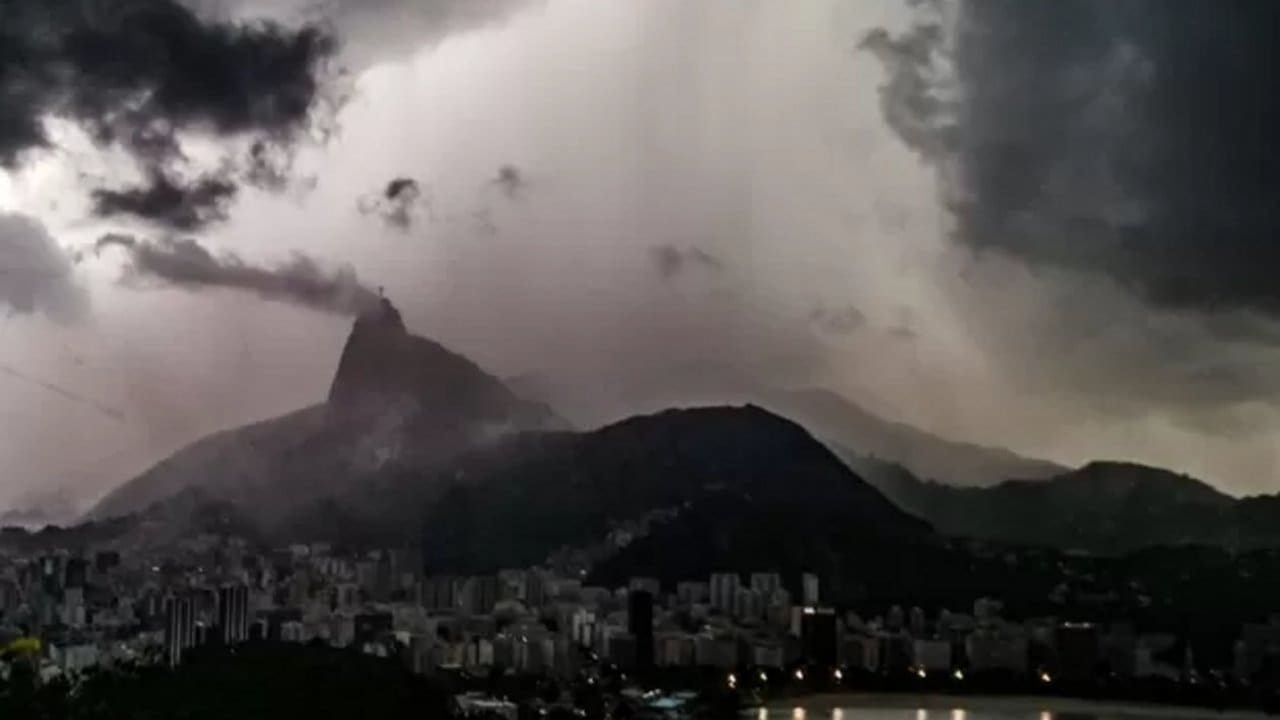Rio de Janeiro sob tempestade, com o Cristo Redentor visível, céu nublado e chuva.