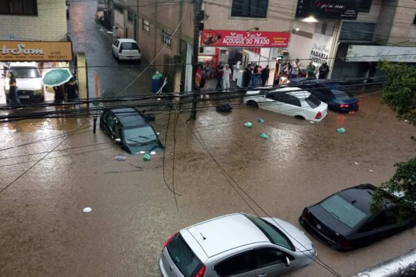 Rua alagada no Rio de Janeiro com carros submersos e pessoas na rua.