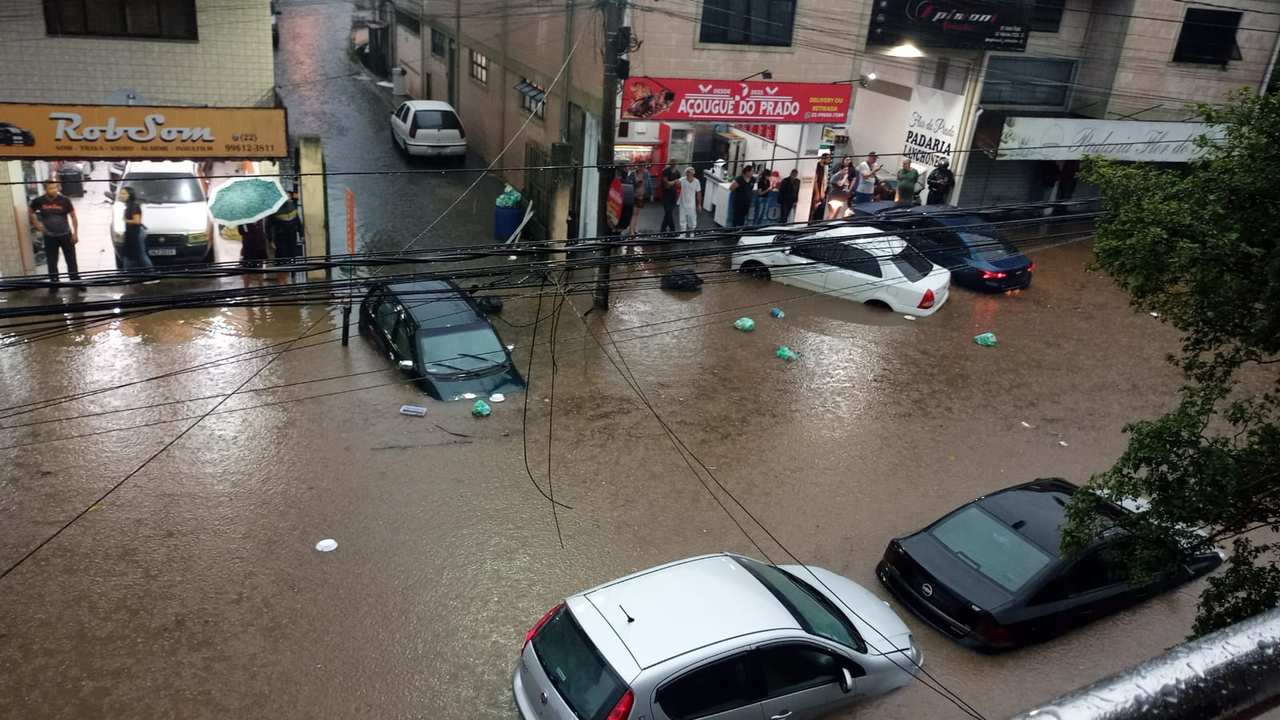 Rua alagada no Rio de Janeiro com carros submersos e pessoas na rua.