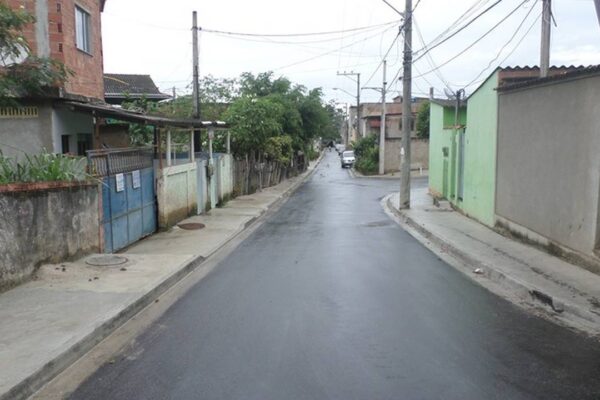 Rua em bairro de Magarça, Rio de Janeiro, com asfalto molhado e casas simples.
