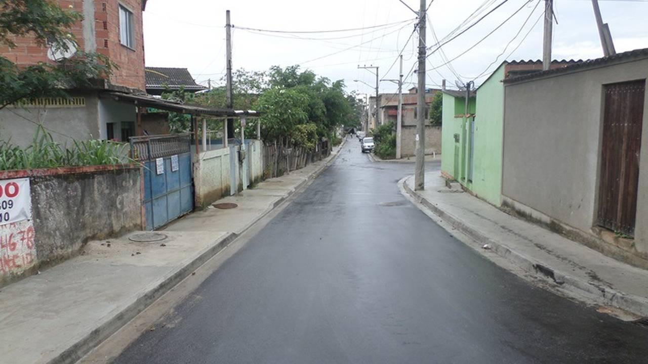 Rua em bairro de Magarça, Rio de Janeiro, com asfalto molhado e casas simples.