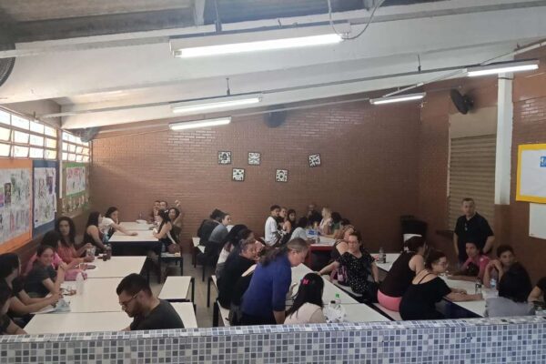 Sala com pessoas sentadas em mesas, possivelmente em reunião ou protesto.