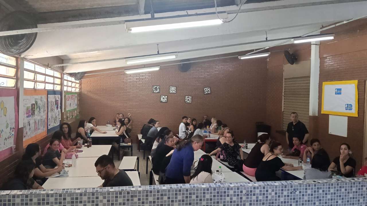 Sala com pessoas sentadas em mesas, possivelmente em reunião ou protesto.