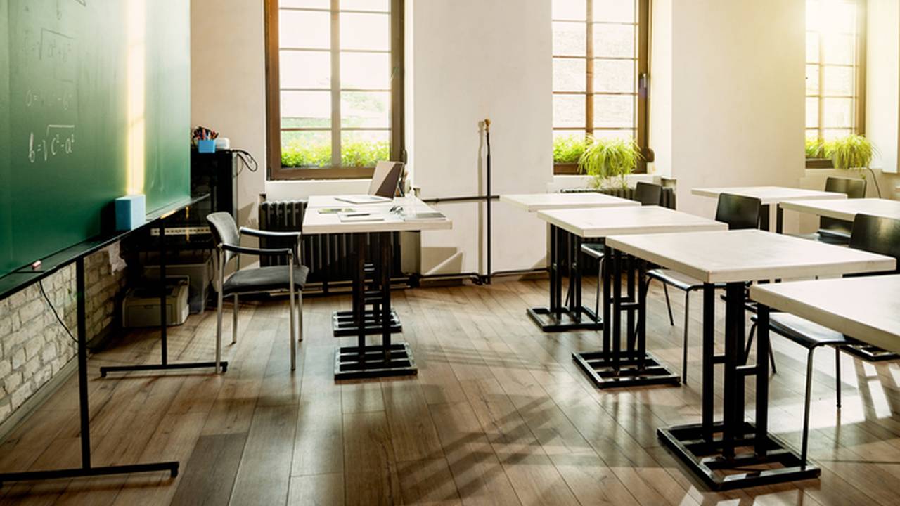 Sala de aula vazia com lousa e mesas, possivelmente em contexto de denúncia.