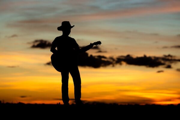 Silhueta de homem tocando violão no pôr do sol, representando artistas do sertanejo.