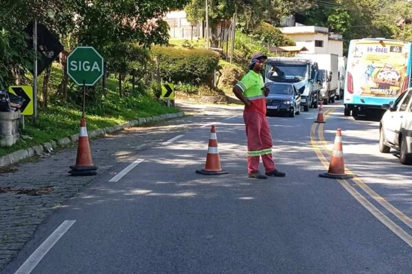 Sinalização de trânsito em obra na Rota 116, com trabalhador orientando o fluxo de veículos.