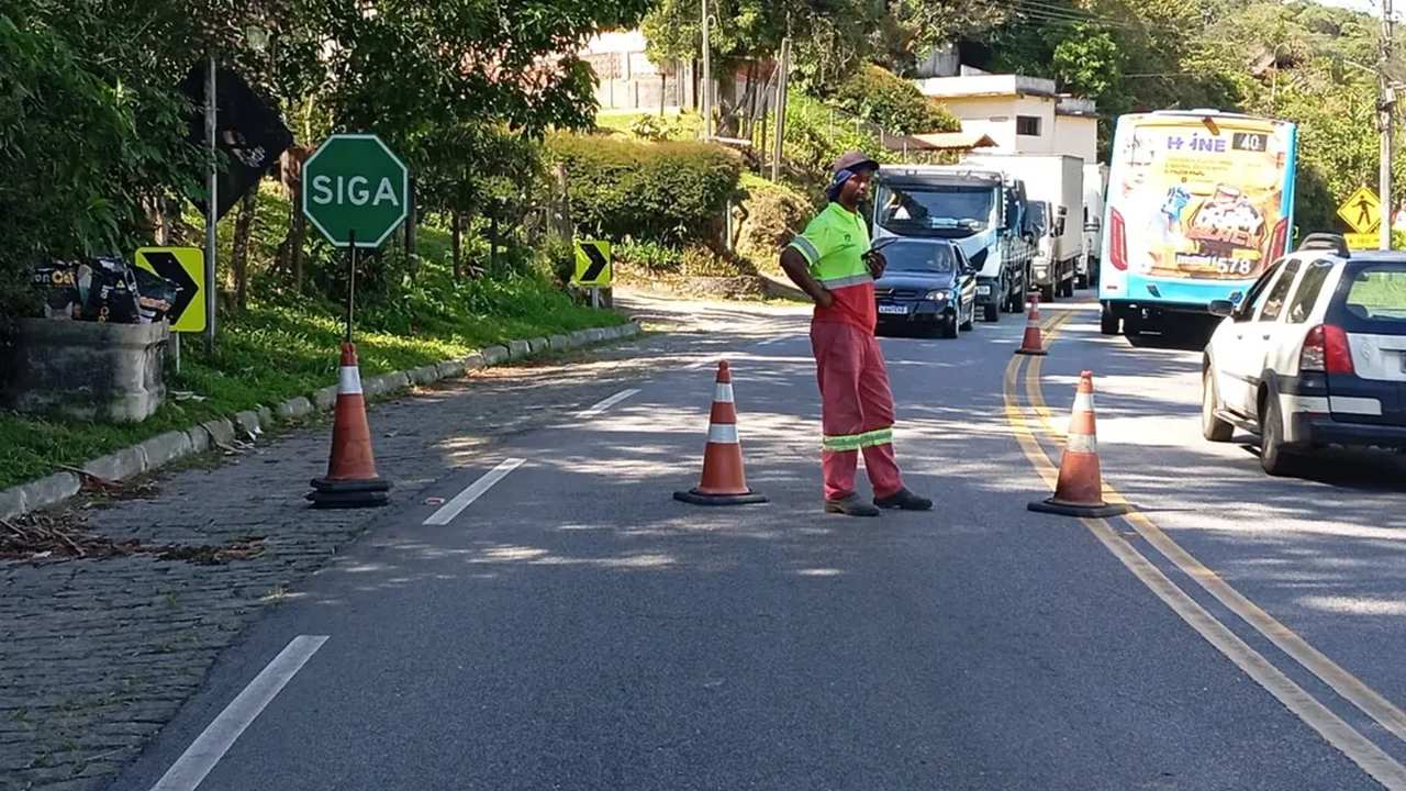 Sinalização de trânsito em obra na Rota 116, com trabalhador orientando o fluxo de veículos.