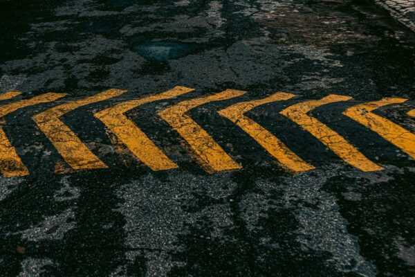 Sinalização horizontal de trânsito: setas amarelas em asfalto escuro indicando direção.