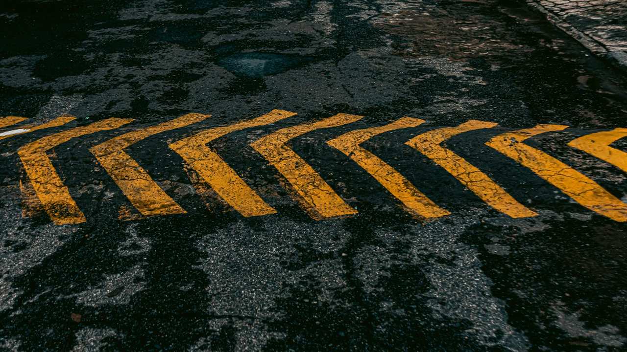 Sinalização horizontal de trânsito: setas amarelas em asfalto escuro indicando direção.