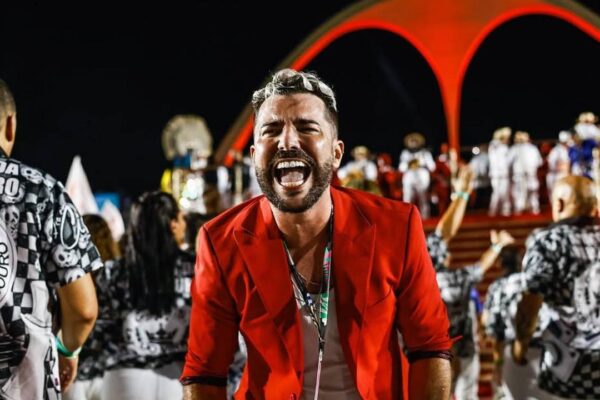 Tarcísio Zanon celebra vitória no Carnaval pela Viradouro, com blazer vermelho e sorriso vibrante.