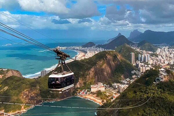 Teleférico no Rio de Janeiro com vista panorâmica da cidade e praias, em dia ensolarado com céu azul e nuvens.