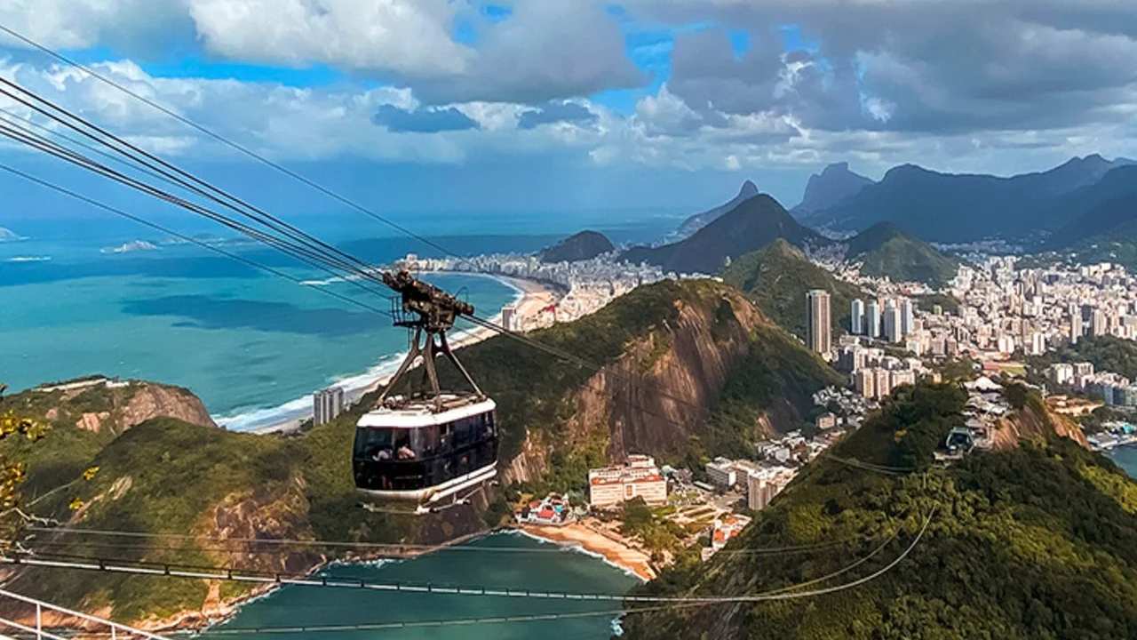 Teleférico no Rio de Janeiro com vista panorâmica da cidade e praias, em dia ensolarado com céu azul e nuvens.