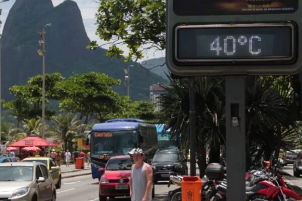 Termômetro digital marca 40°C em rua do Rio de Janeiro, com ônibus, carros e montanhas ao fundo.