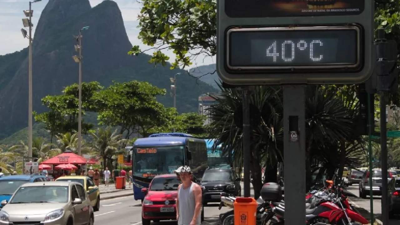 Termômetro digital marca 40°C em rua do Rio de Janeiro, com ônibus, carros e montanhas ao fundo.