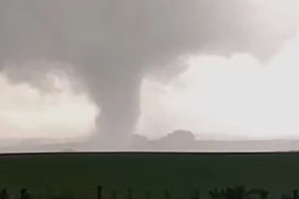 Tornado passando por uma área rural no Rio Grande do Sul, com céu nublado e uma grande coluna de ar girando em direção ao chão.