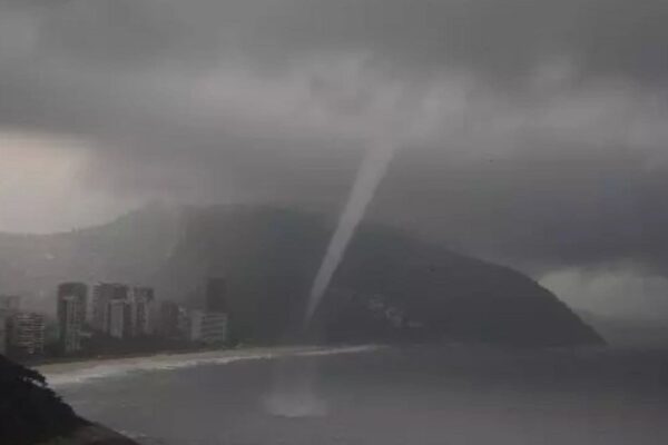 Tornado sobre a praia no Rio de Janeiro durante tempestade, com prédios e morro ao fundo.