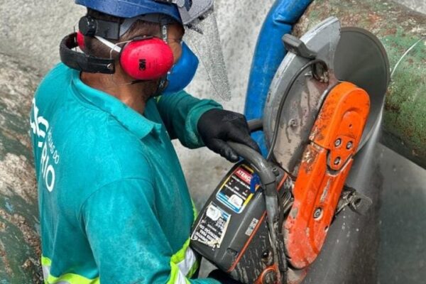 Trabalhador cortando tubo para reparo em sistema de água no Rio de Janeiro, com equipamentos de segurança