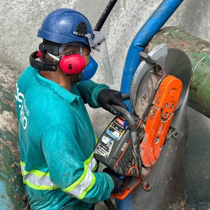 Trabalhador cortando tubo para reparo em sistema de água no Rio de Janeiro, com equipamentos de segurança