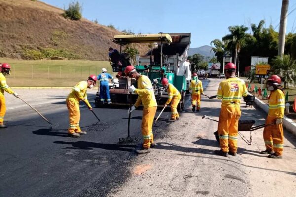 Trabalhadores em uma obra de recapeamento asfáltico de uma estrada, usando ferramentas e um caminhão