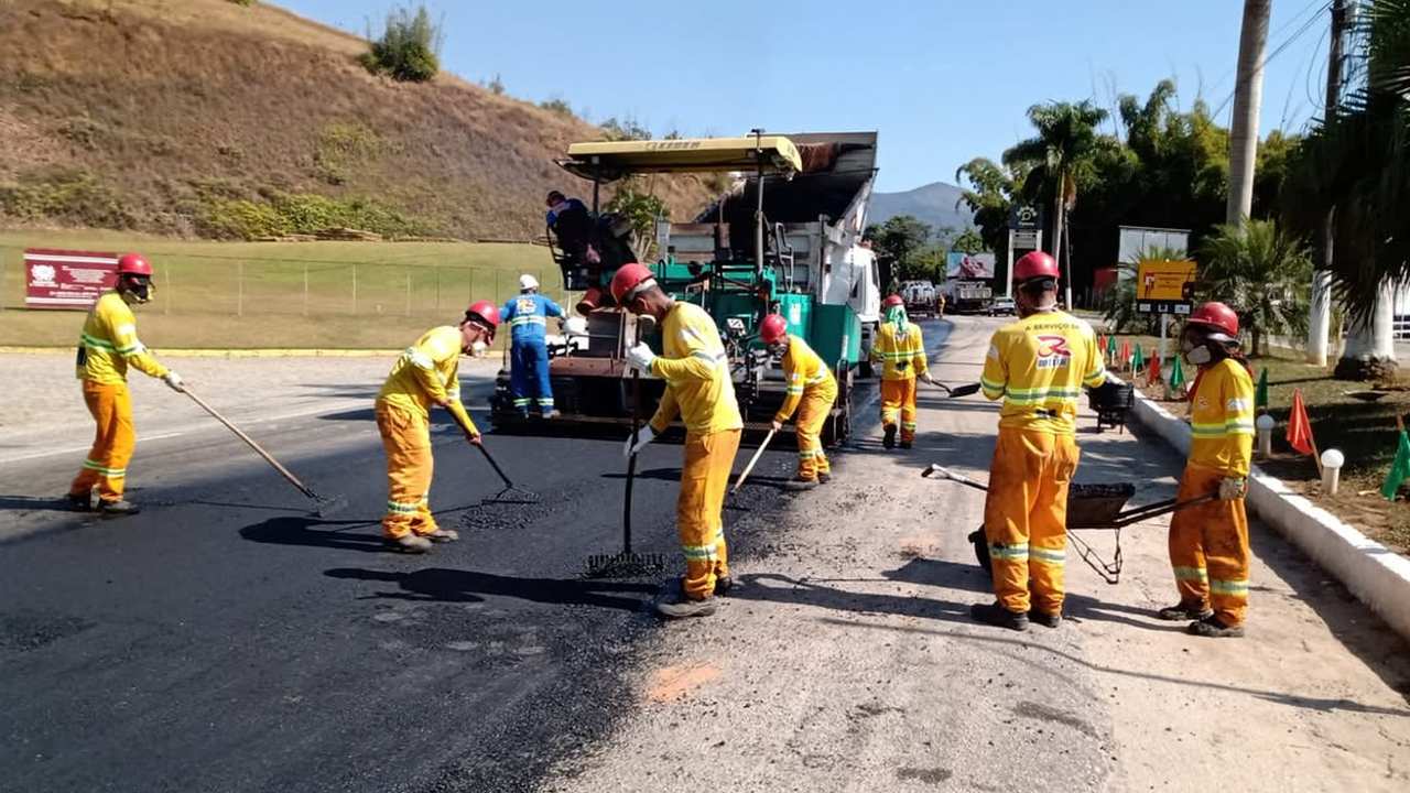 Trabalhadores em uma obra de recapeamento asfáltico de uma estrada, usando ferramentas e um caminhão