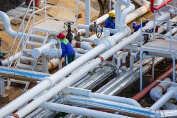 Trabalhadores em uniforme em uma planta industrial, com tubulações e equipamentos de água.