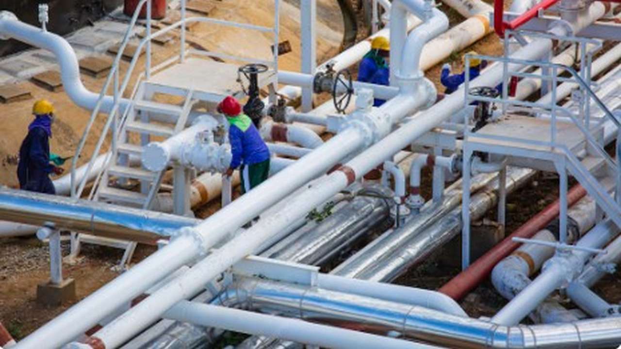 Trabalhadores em uniforme em uma planta industrial, com tubulações e equipamentos de água.