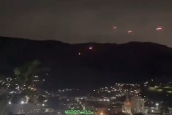 Traçantes no céu noturno sobre favelas do Rio de Janeiro, possivelmente em confronto entre facções criminosas.