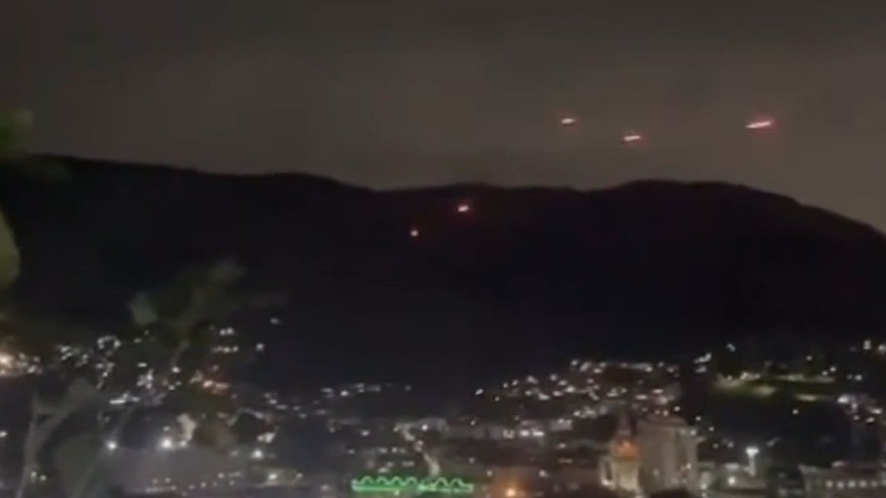 Traçantes no céu noturno sobre favelas do Rio de Janeiro, possivelmente em confronto entre facções criminosas.