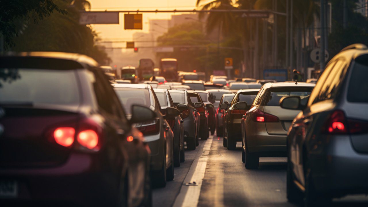 Trânsito intenso de carros em rua do Rio de Janeiro, com luz do sol no fim da tarde.