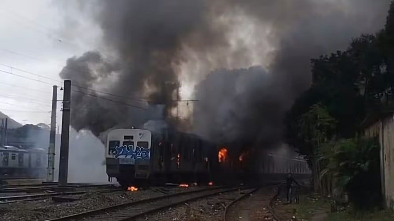 Trem em chamas em pátio da estação Japeri, com fumaça densa.
