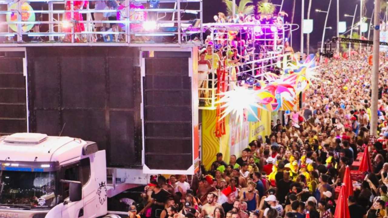 Trio elétrico em evento, com multidão de pessoas na rua.