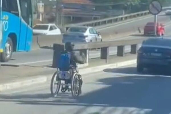 Um cadeirante em uma cadeira de rodas motorizada, em Niterói, dirige entre carros em uma via movimentada.