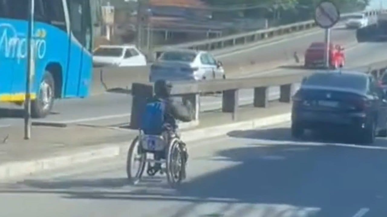 Um cadeirante em uma cadeira de rodas motorizada, em Niterói, dirige entre carros em uma via movimentada.