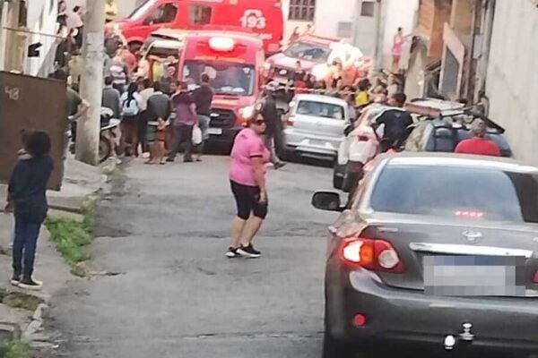 Um caminhão de bombeiros estacionado em uma rua estreita com pessoas reunidas e carros ao redor.