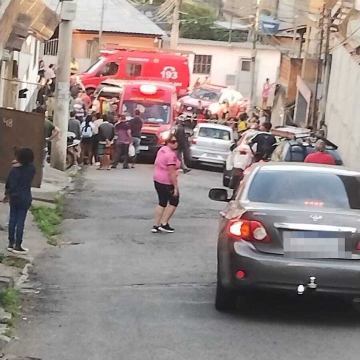 Um caminhão de bombeiros estacionado em uma rua estreita com pessoas reunidas e carros ao redor.