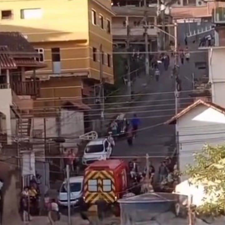 Uma cena caótica com vários carros, um caminhão de bombeiros e pessoas reunidas em uma rua de paralelepípedos.
