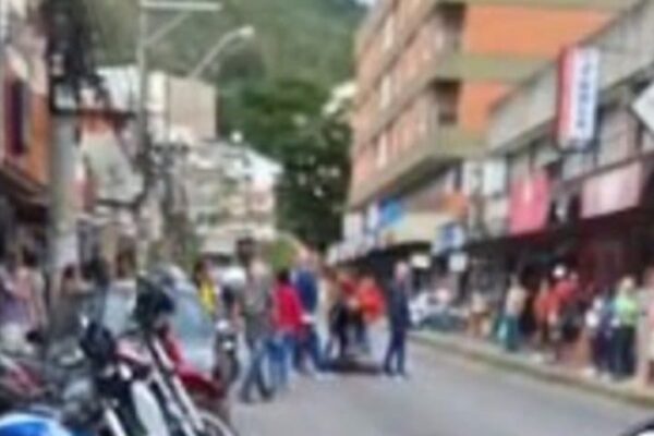 Uma rua com várias motocicletas estacionadas, uma mulher caída no chão e pessoas ao redor, em Nova Friburgo, RJ.