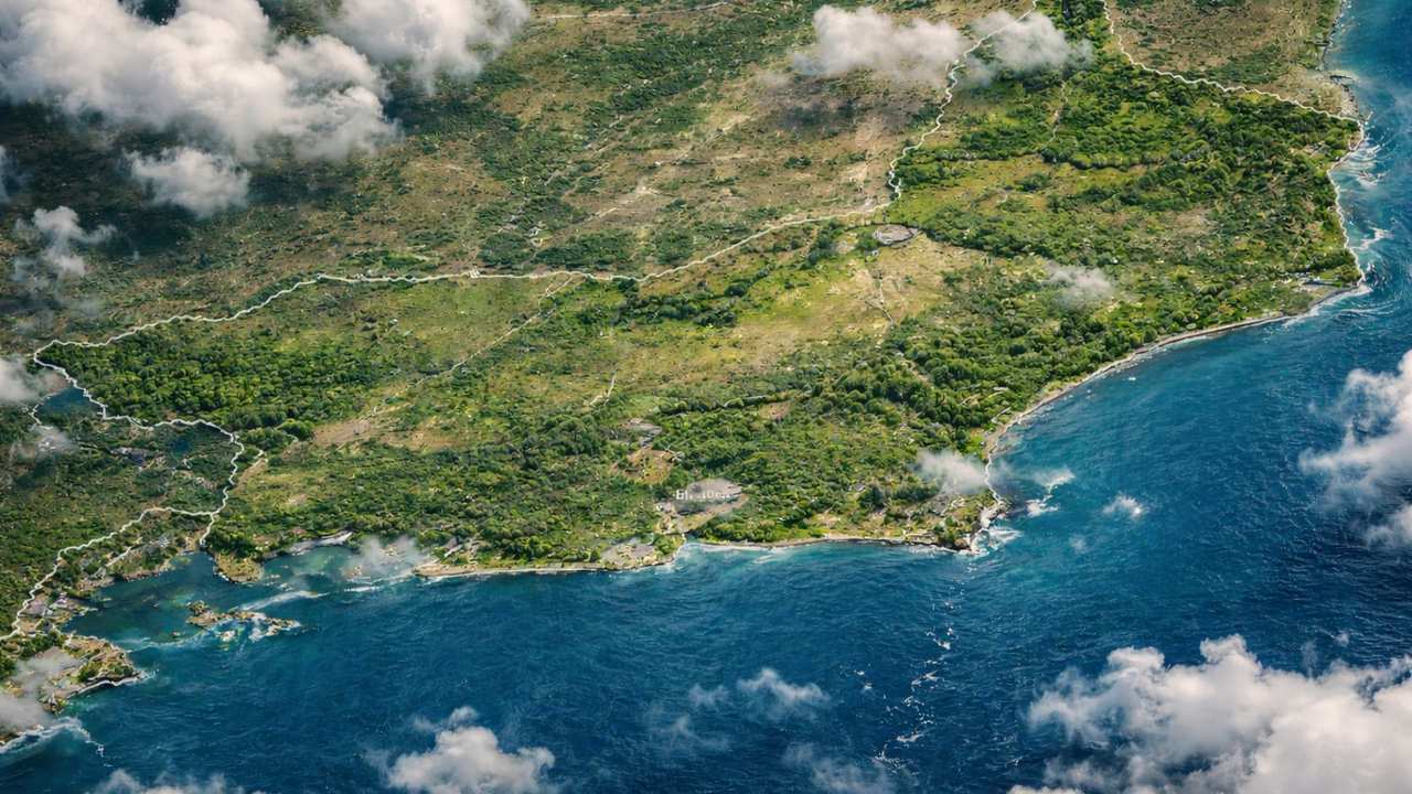 Vista aérea da costa com vegetação densa e mar azul, sob céu parcialmente nublado.