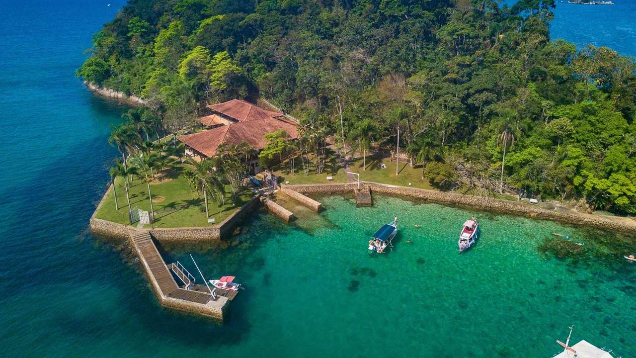 Vista aérea da costa de Paraty com ilha, casas, barcos e águas cristalinas