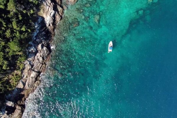 Vista aérea da Ilha dos Papagaios em Cabo Frio, com barco na água turquesa e vegetação.