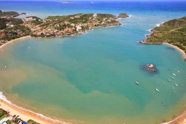 Vista aérea da Praia da Ferradura em Búzios, com areia, água azul e vegetação.