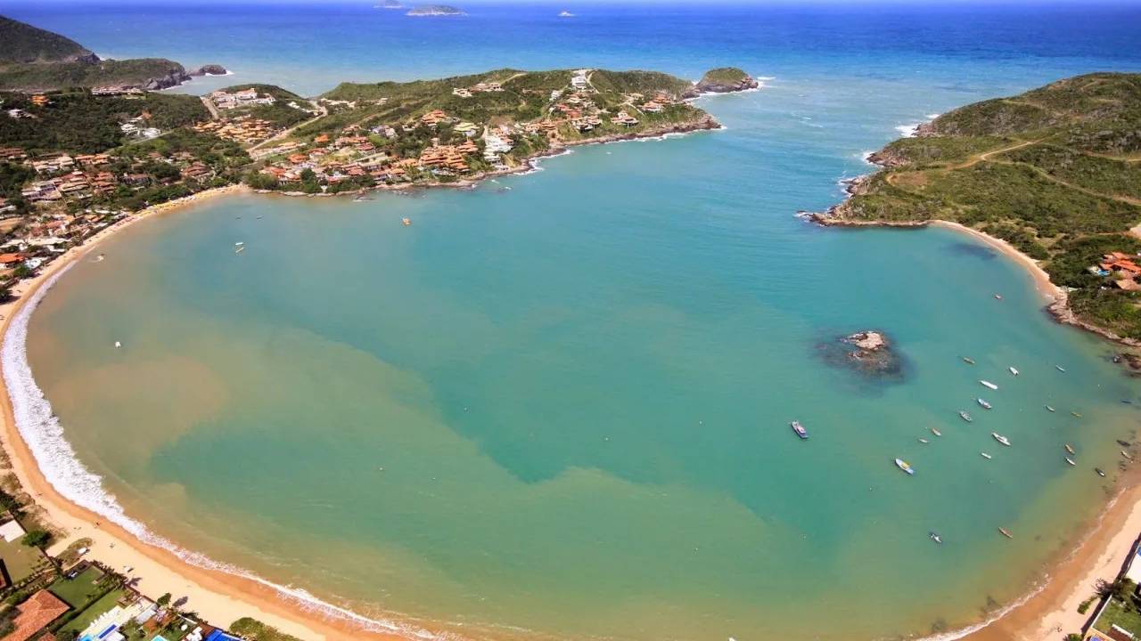 Vista aérea da Praia da Ferradura em Búzios, com areia, água azul e vegetação.