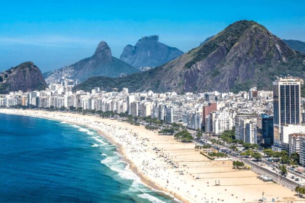 Vista aérea da Praia de Copacabana no Rio de Janeiro, com prédios e montanhas ao fundo.