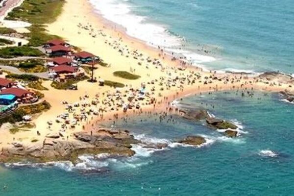 Vista aérea da Praia de Rio das Ostras, com pessoas na areia e quiosques.