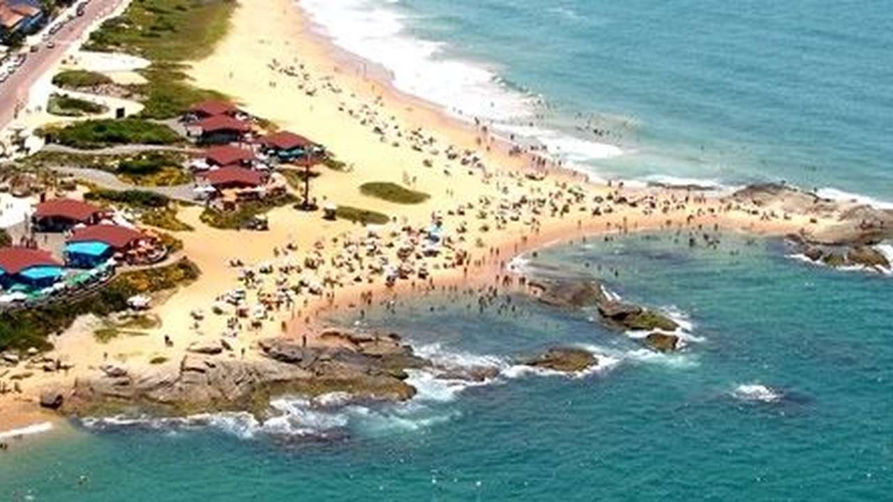 Vista aérea da Praia de Rio das Ostras, com pessoas na areia e quiosques.