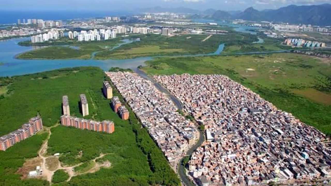 Vista aérea de favela Rio das Pedras em Muzema, Rio de Janeiro, com prédios ao lado e natureza ao fundo.