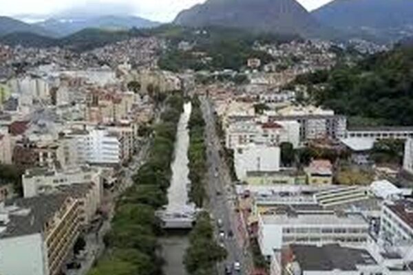 Vista aérea de Nova Friburgo, cidade na região serrana do Rio de Janeiro, com montanhas ao fundo e rio no meio.